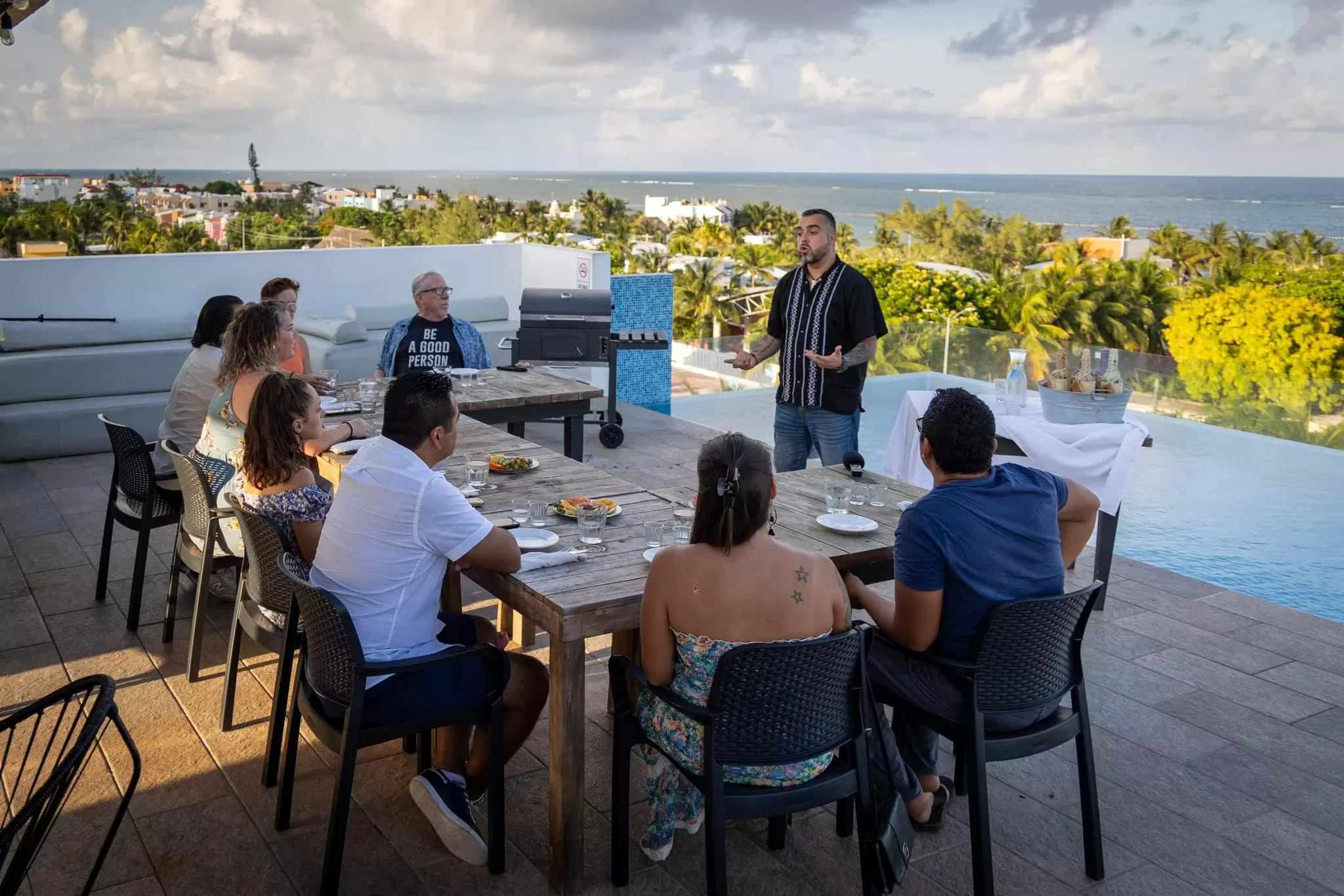 A group of people gathered around the table on the rooftop of Osteria Barocca next to the infinity pool with ocean views in the background.