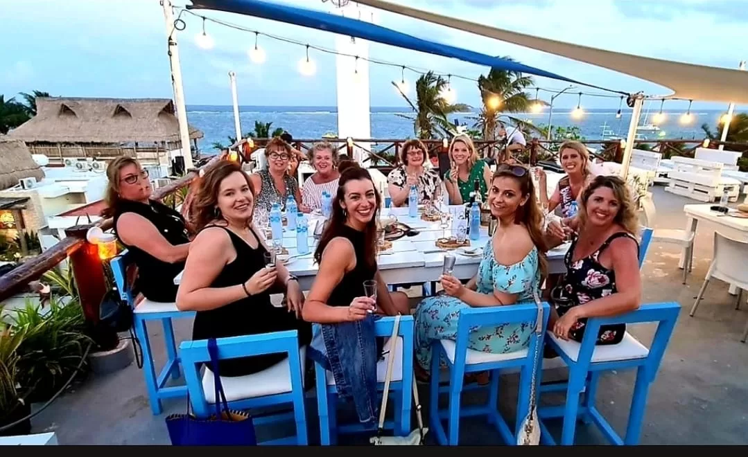 A group of women sitting on blue chairs around a table on the rooftop at La Sirena overlooking the ocean.