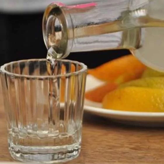 Mezcal being poured from a clear glass bottle into a clear glass shot glass.