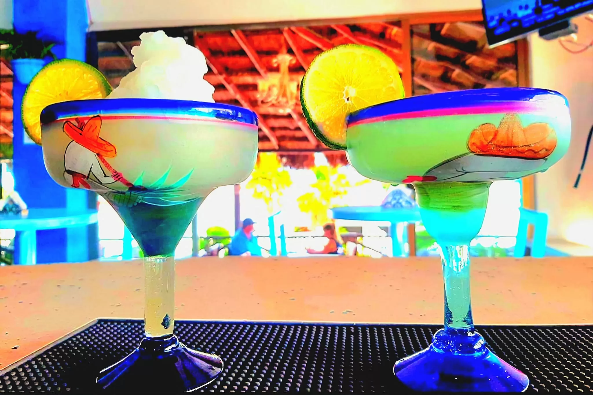 Two margaritas on the counter at La Sirena in Puerto Morelos, served in handpainted margarita glasses featuring traditional Mexican themes.