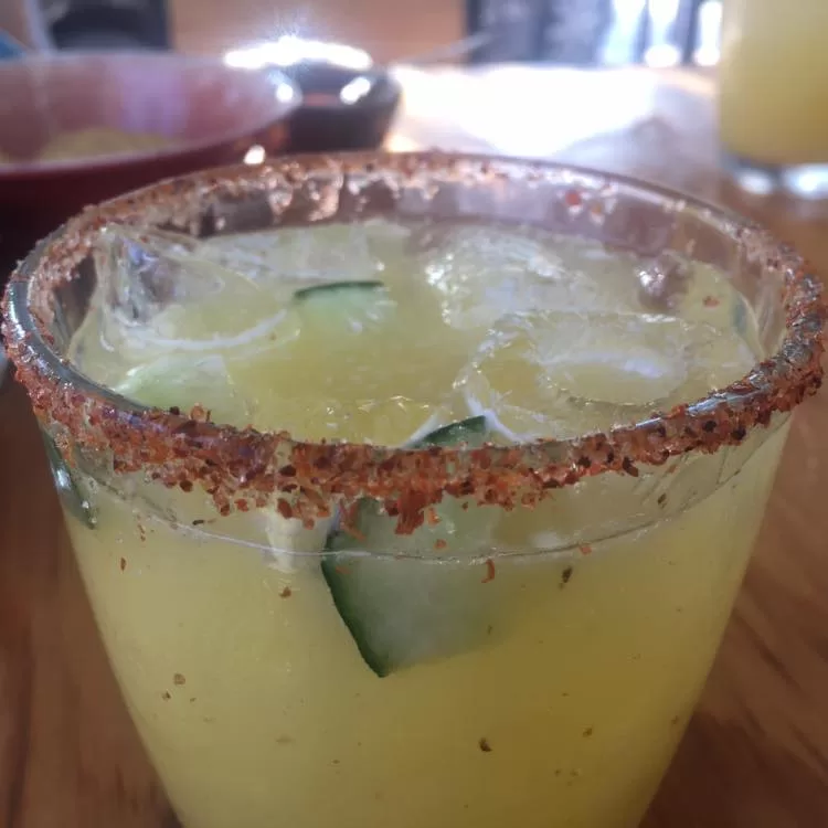 A glass rimmed with tajin and filled with ice cubes and a light yellow mezcalina cocktail.