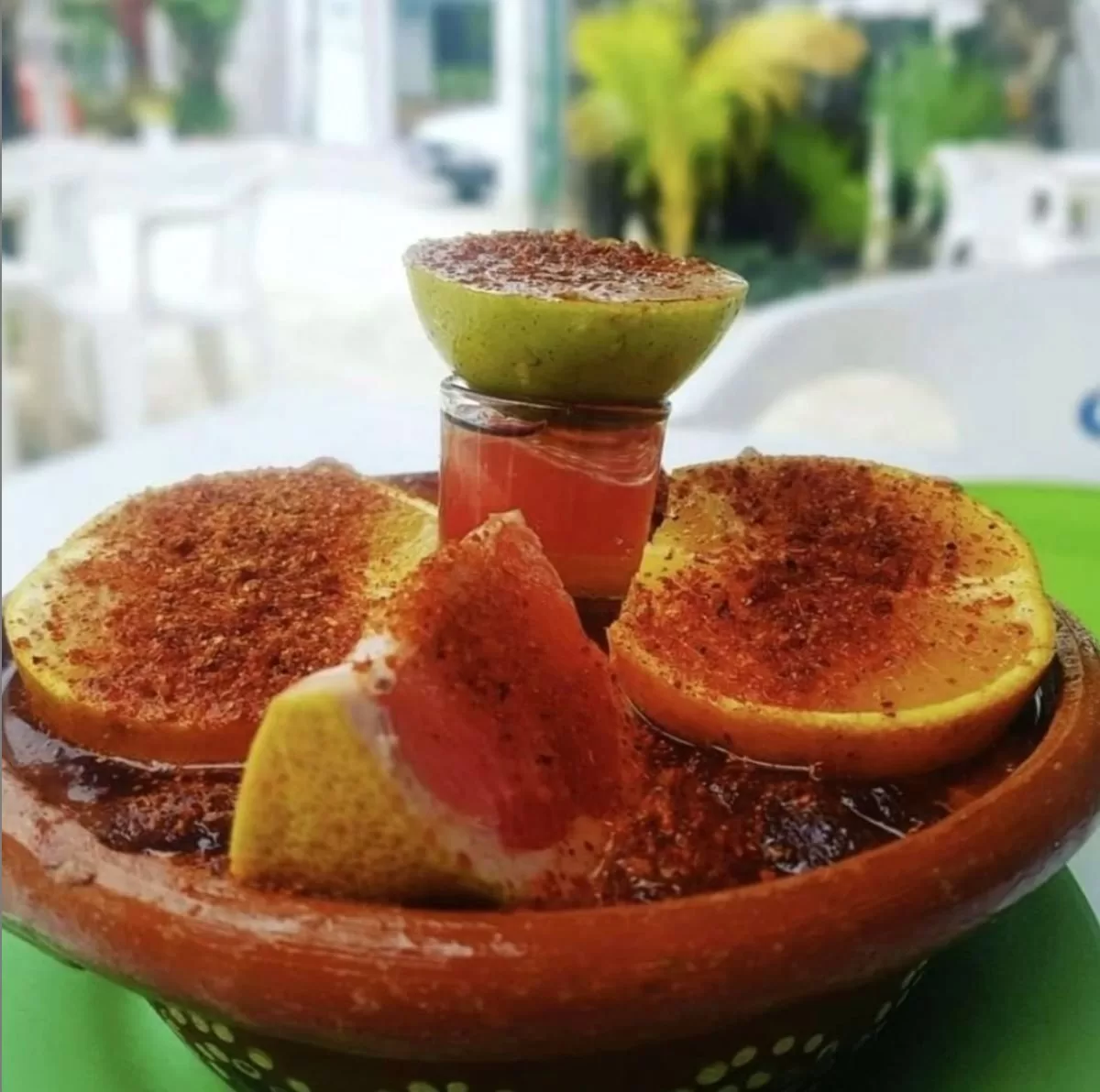 Slices of citrus fruits topped with tajin floating in a shallow clay dish filled with tequila and lime, grapefruit, and orange juices.