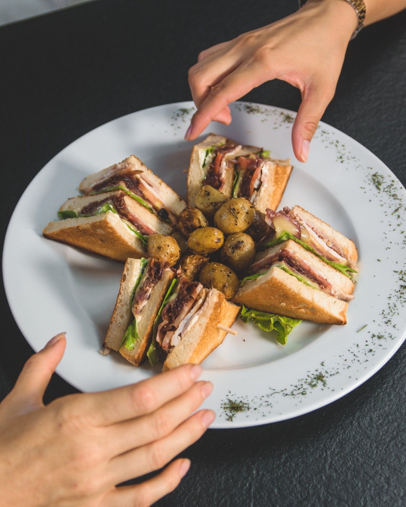 A club sandwich at Belleville, cut into four sections. Two people are each reaching out one hand to pick up a piece off the plate.
