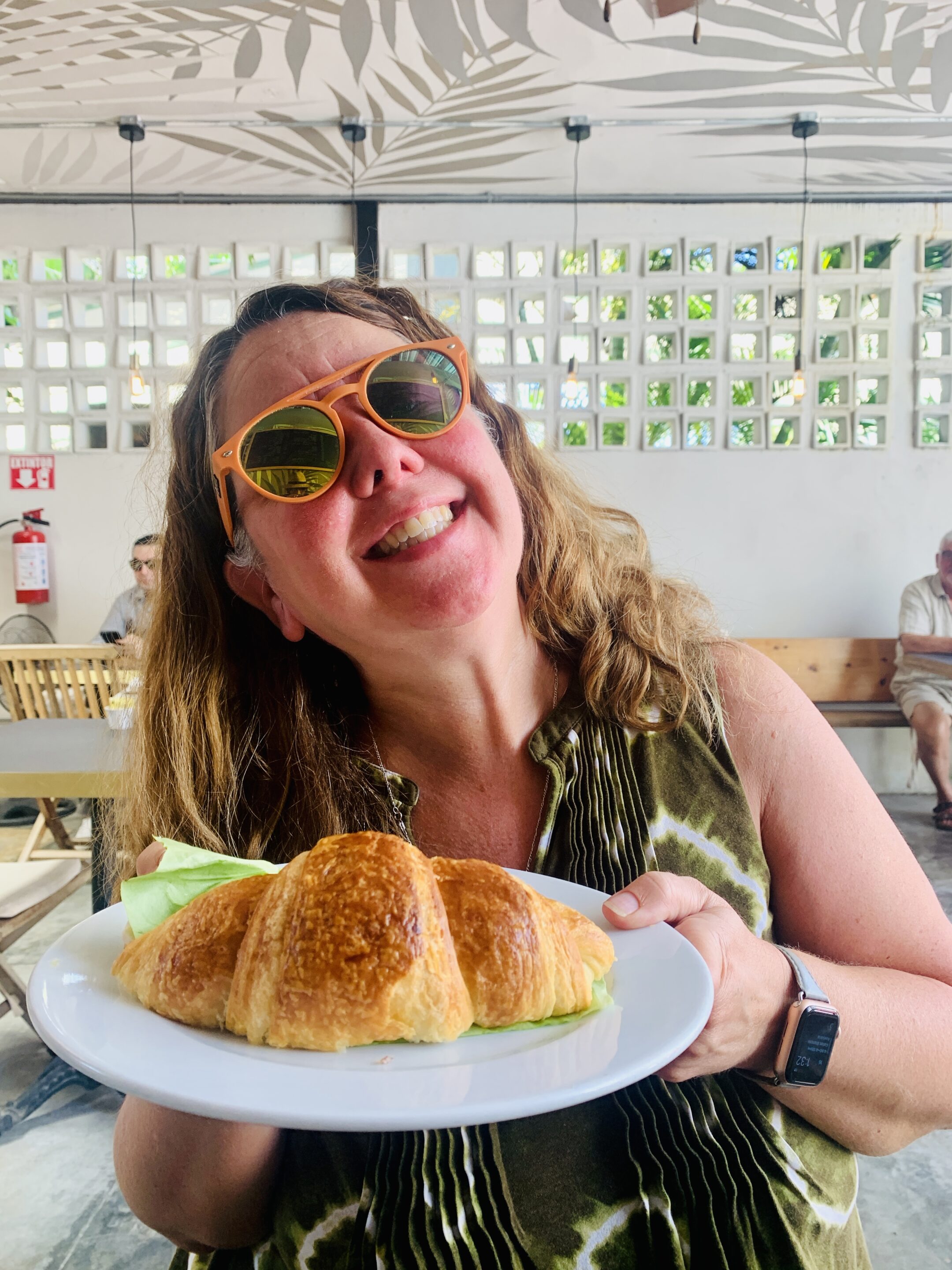 XPM Co-founder Bridget Espinosa at Belleville French Bakery in Puerto Morelos with a large croissant on a dinner plate.