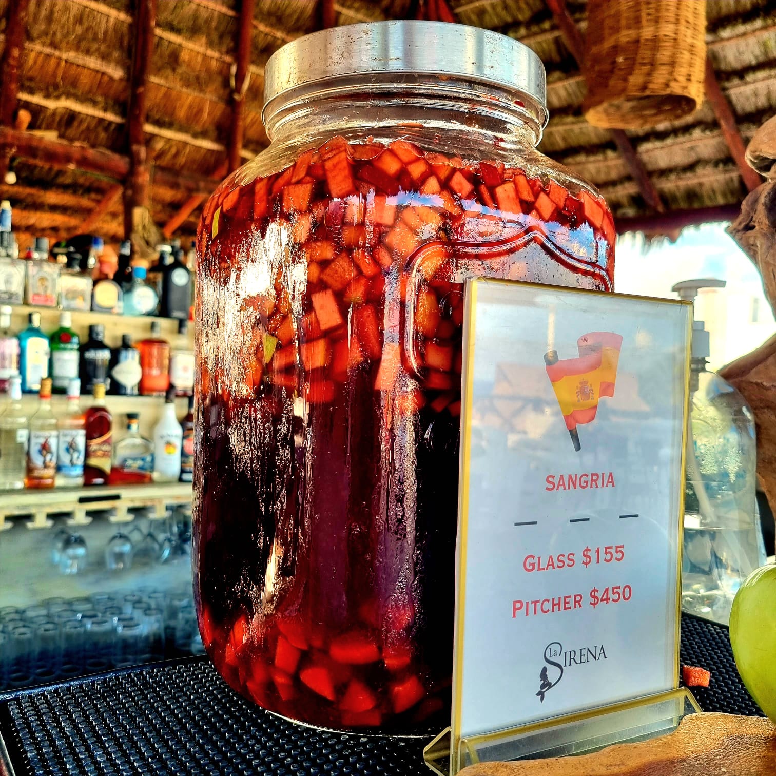 A large glass beverage container filled with sangria and fruit with a sign labeling the contents bearing the Spanish flag.
