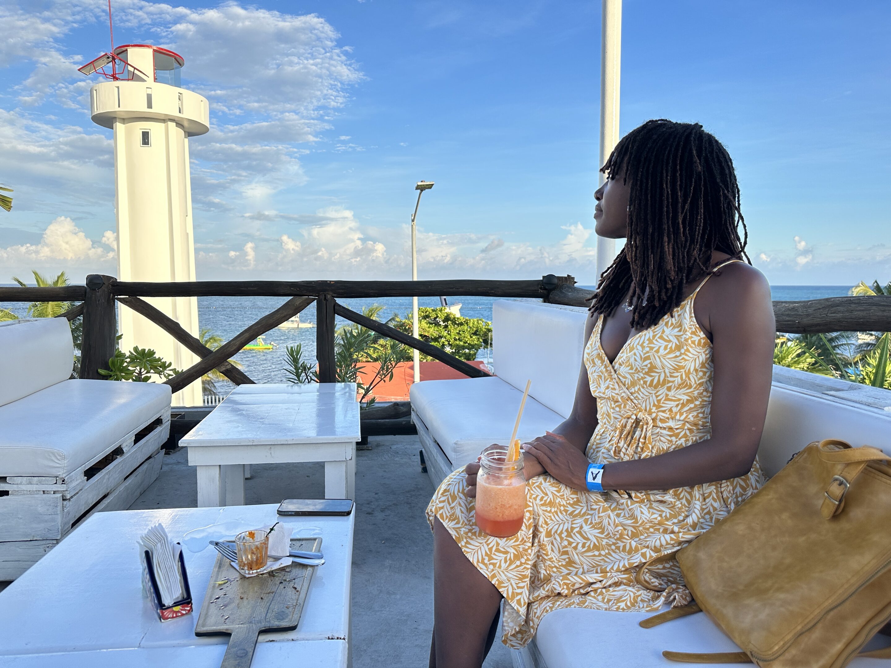 A woman sitting on the rooftop at La Sirena enjoying a cocktail and the view of the lighthouse and the ocean in the background.