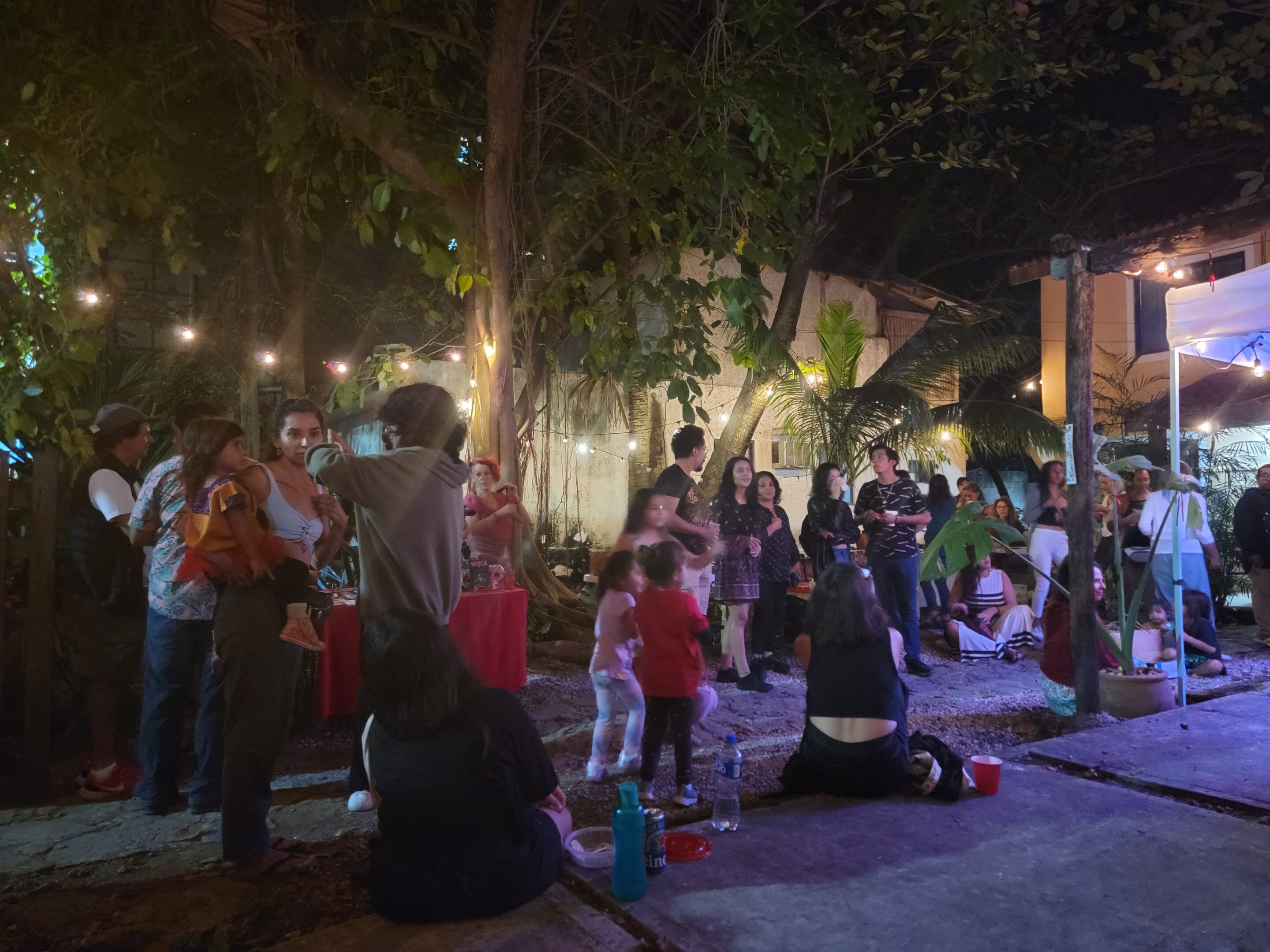 Group of people sitting and standing, while talking and listening to a variety of performances during the "Weaving Community" Christmas Posada with El Telar and Experience Puerto Morelos.