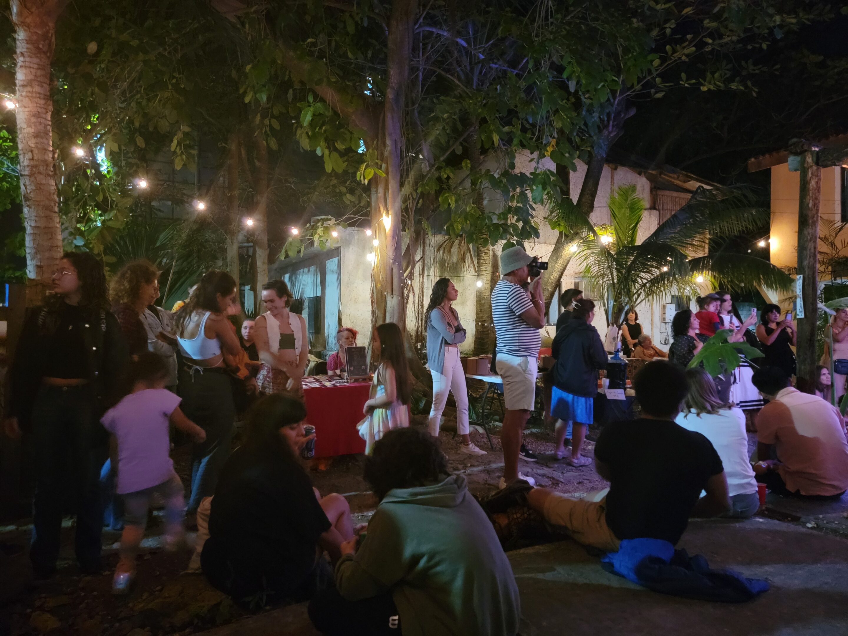 Group of people sitting and standing, while talking and listening to a variety of performances during the "Weaving Community" Christmas Posada with El Telar and Experience Puerto Morelos.