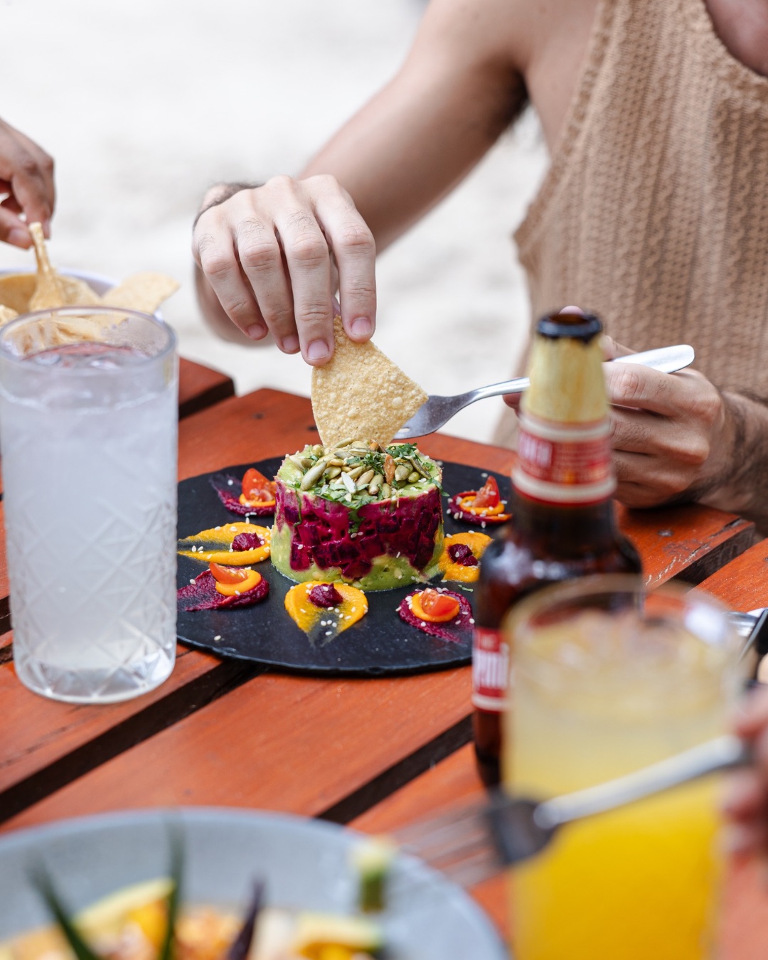 A person using a tortilla chip to scoop up some of Unico Beach Club's delicious and colorful beet guacamole.