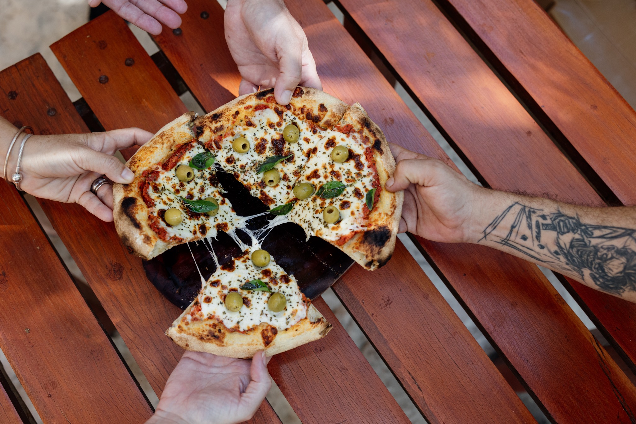 Hands of 4 people each taking a slice of vegetarian pizza at Unico Beach Club in Puerto Morelos.