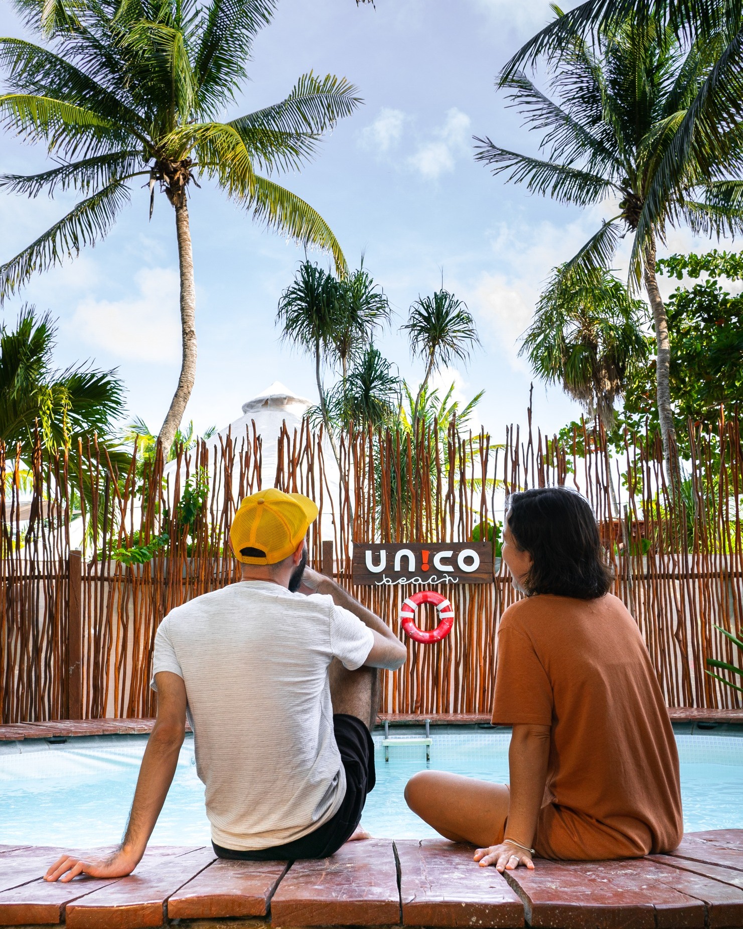 A couple sits on the edge of the pool at Unico Beach Club in Puerto Morelos with their feet in the water.