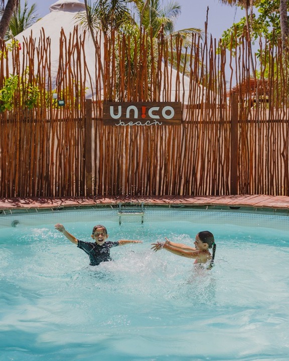 Two children splash in the blue water of the pool at Unico Beach Club.